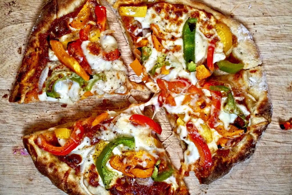A baked sourdough pizza crust baked with melted cheese and multi colored peppers